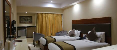 A hotel room with two beds, a desk, a chair, a ceiling fan, and a painting on the wall.