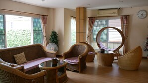 Sala de estar com móveis de vime, mesa de vidro e grandes janelas com cortinas.
