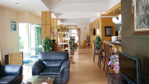 Uma sala de estar moderna com um sofá de couro, uma mesa de centro de vidro e uma televisão. Há armários de madeira e uma estante de livros com livros e objetos decorativos.