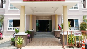 Entrada de hotel com placa vermelha, cobertura e vasos de plantas.