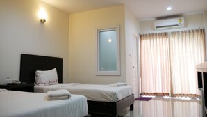 Quarto de hotel com duas camas, uma mesa de cabeceira, ar condicionado fixado na parede e uma janela com cortinas.
