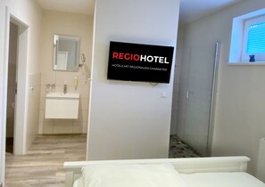 A hotel room with a bed, a bathroom with a sink and mirror, and a wall-mounted TV displaying 'REGIOHOTEL'. - Regiohotel Berghotel Ilsenburg (Ilsenburg)
