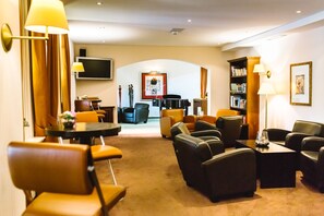 A hotel lobby with leather sofas, a piano, a bookshelf, and a flat-screen TV. - Regiohotel Berghotel Ilsenburg (Ilsenburg)
