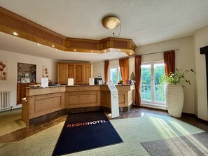 A hotel lobby with wooden cabinetry, a reception desk, and a large window with curtains. - Regiohotel Berghotel Ilsenburg (Ilsenburg)