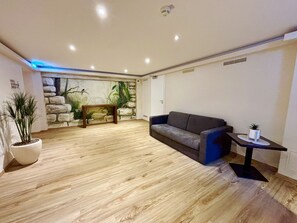 A modern living room with a wooden floor, a grey sofa, a small table with a plant, and a stone wall mural.