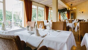 A restaurant with white tablecloths, wicker chairs, and a view of greenery outside. - Regiohotel Berghotel Ilsenburg (Ilsenburg)