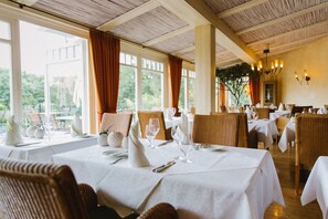 A restaurant with white tablecloths, wicker chairs, and a view of greenery outside. - Regiohotel Berghotel Ilsenburg (Ilsenburg)