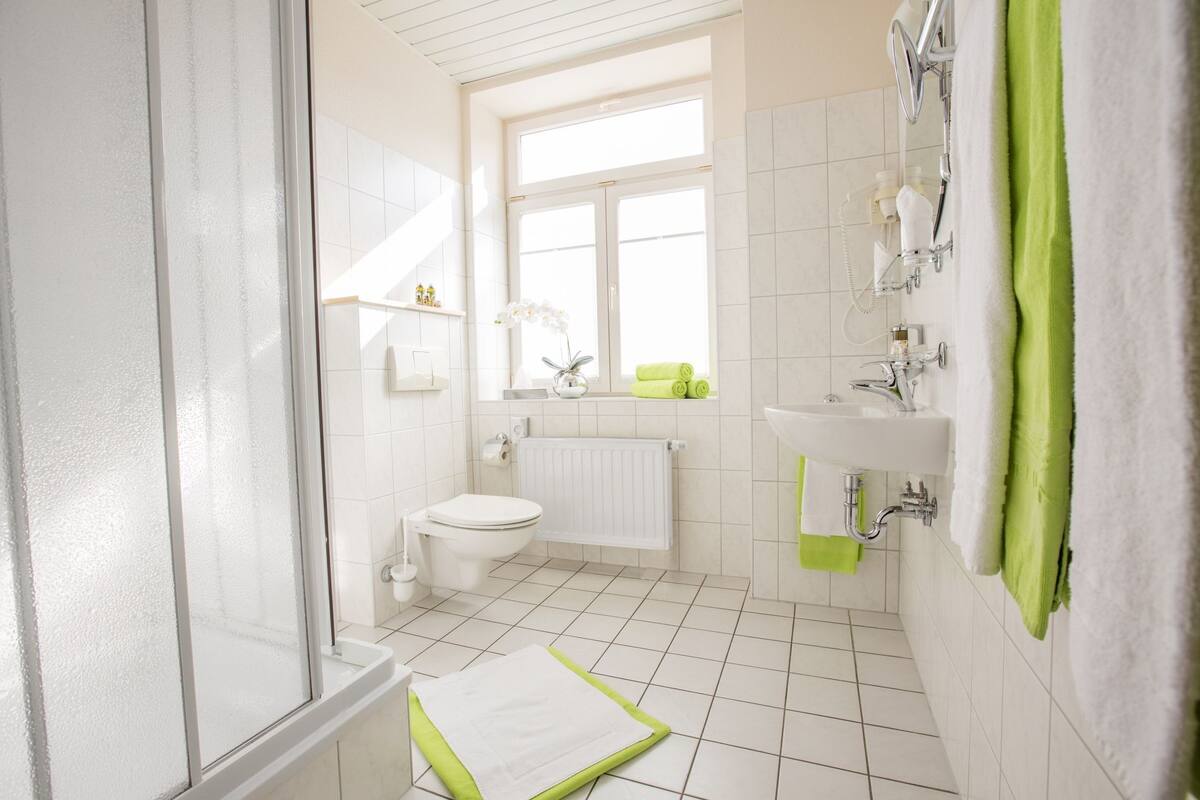 Un ba ño moderno con ducha, inodoro y lavamanos, que cuenta con un ventanal grande y una toalla verde.