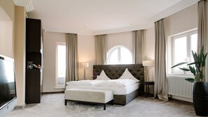A hotel bedroom with a large bed, a TV, a potted plant, and a window with curtains. - Regiohotel Berghotel Ilsenburg (Ilsenburg)