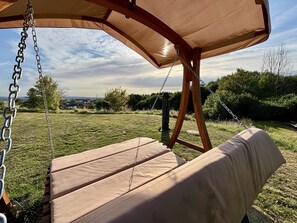 A wooden swing with a canopy, set in a grassy outdoor area with a view of the sky and distant buildings. - Regiohotel Berghotel Ilsenburg (Ilsenburg)