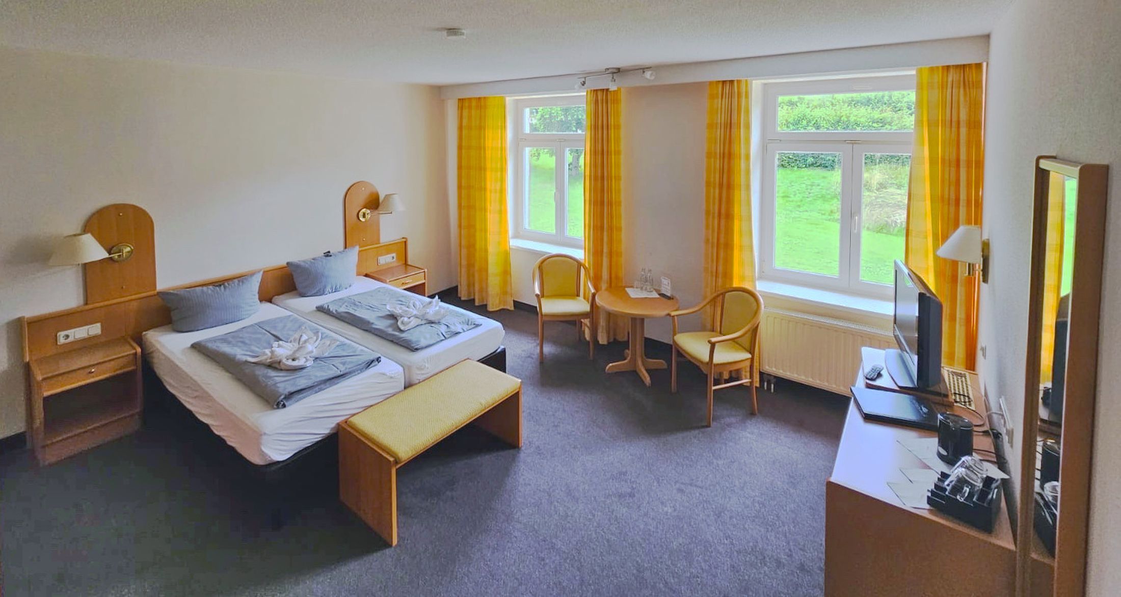 Habitación de hotel con dos camas, un escritorio, una silla, un televisor y una ventana con cortinas.