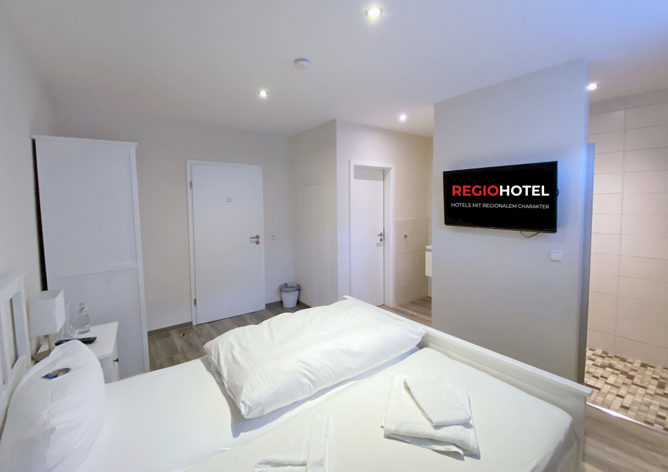 Une chambre d’hôtel avec un lit, un téléviseur fixé au mur et une porte donnant sur une salle de bain.