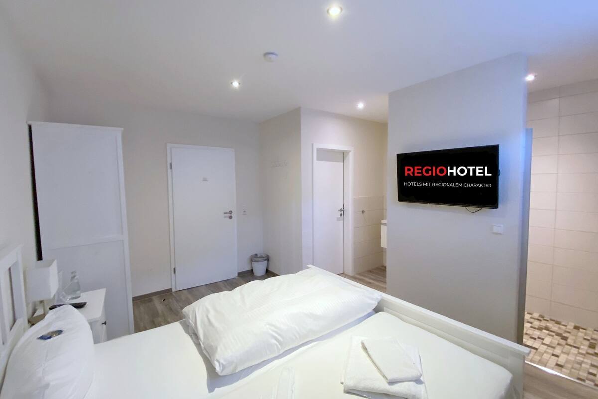 Habitación de hotel con cama, televisión montada en la pared y puerta que da a un baño.