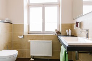 A bathroom with a toilet, a sink, a window, and a towel rack. - Regiohotel Berghotel Ilsenburg (Ilsenburg)