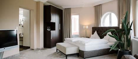 A hotel room with a bed, a TV, a plant, and a view of the outside.