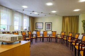 Un salón de conferencias con proyector, varias sillas, una mesa y cuadros en la pared.