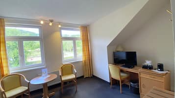A hotel room with a desk, two chairs, a television, and a small table.