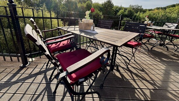An outdoor patio with a wooden table and chairs, surrounded by a metal railing. - Regiohotel Berghotel Ilsenburg (Ilsenburg)