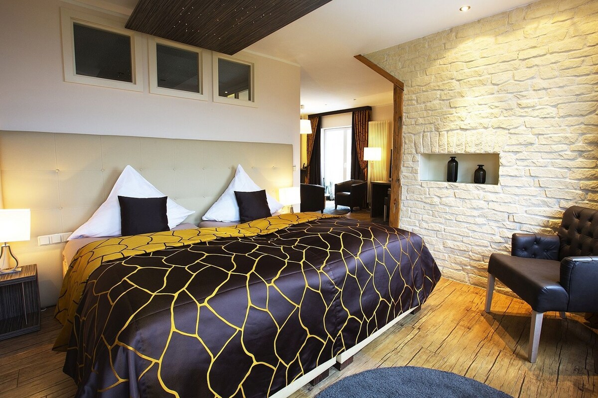 A hotel room with a large bed, a stone accent wall, a seating area, and a view of the room.