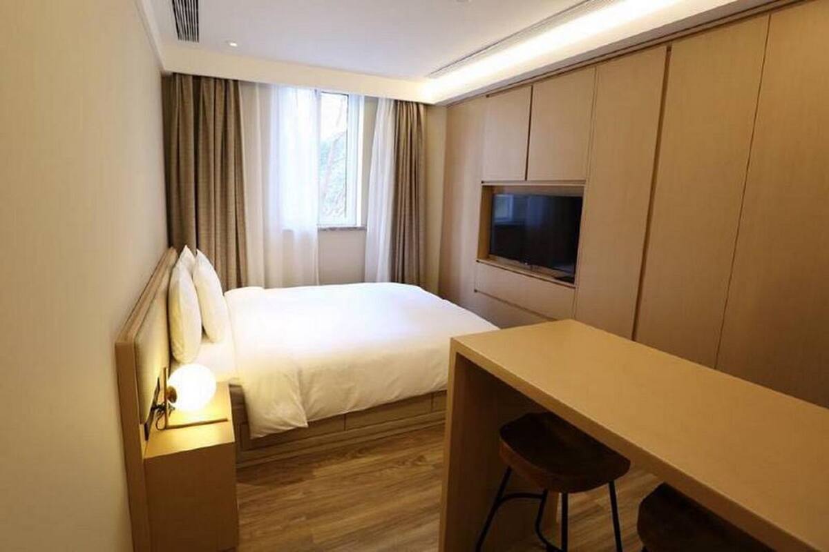 Een hotelkamer met een bed, een bureau, een stoel, een televisie en een raam met gordijnen.