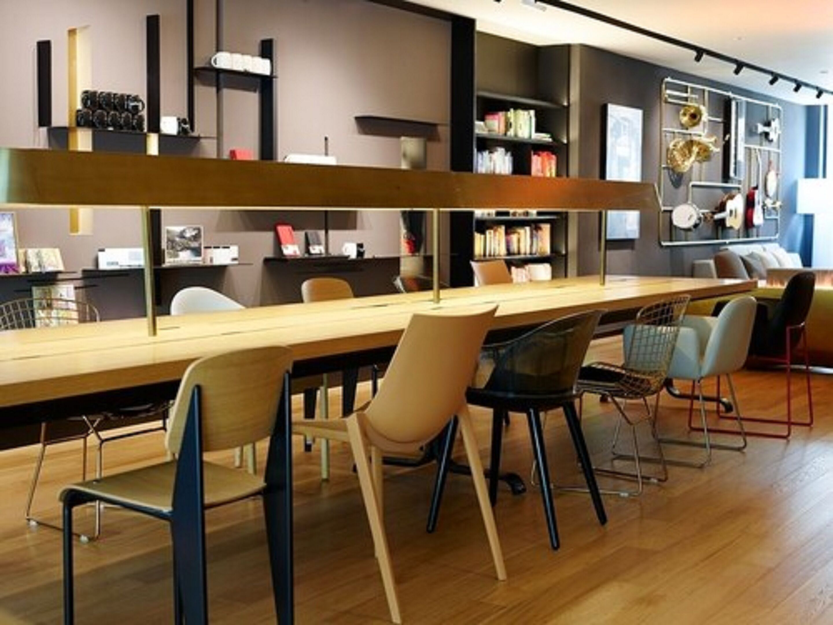 A modern bar area with a long counter, several chairs, and a bookshelf in the background.