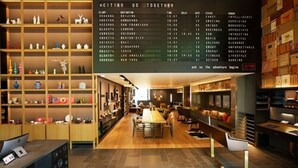 A modern hotel lobby with a central seating area, a large digital flight information board, and a variety of decorative items on shelves.