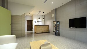 A modern hotel lobby with a reception desk, a flat-screen TV, and a seating area with a table and chairs. - GOODHOUSE (Hengchun)