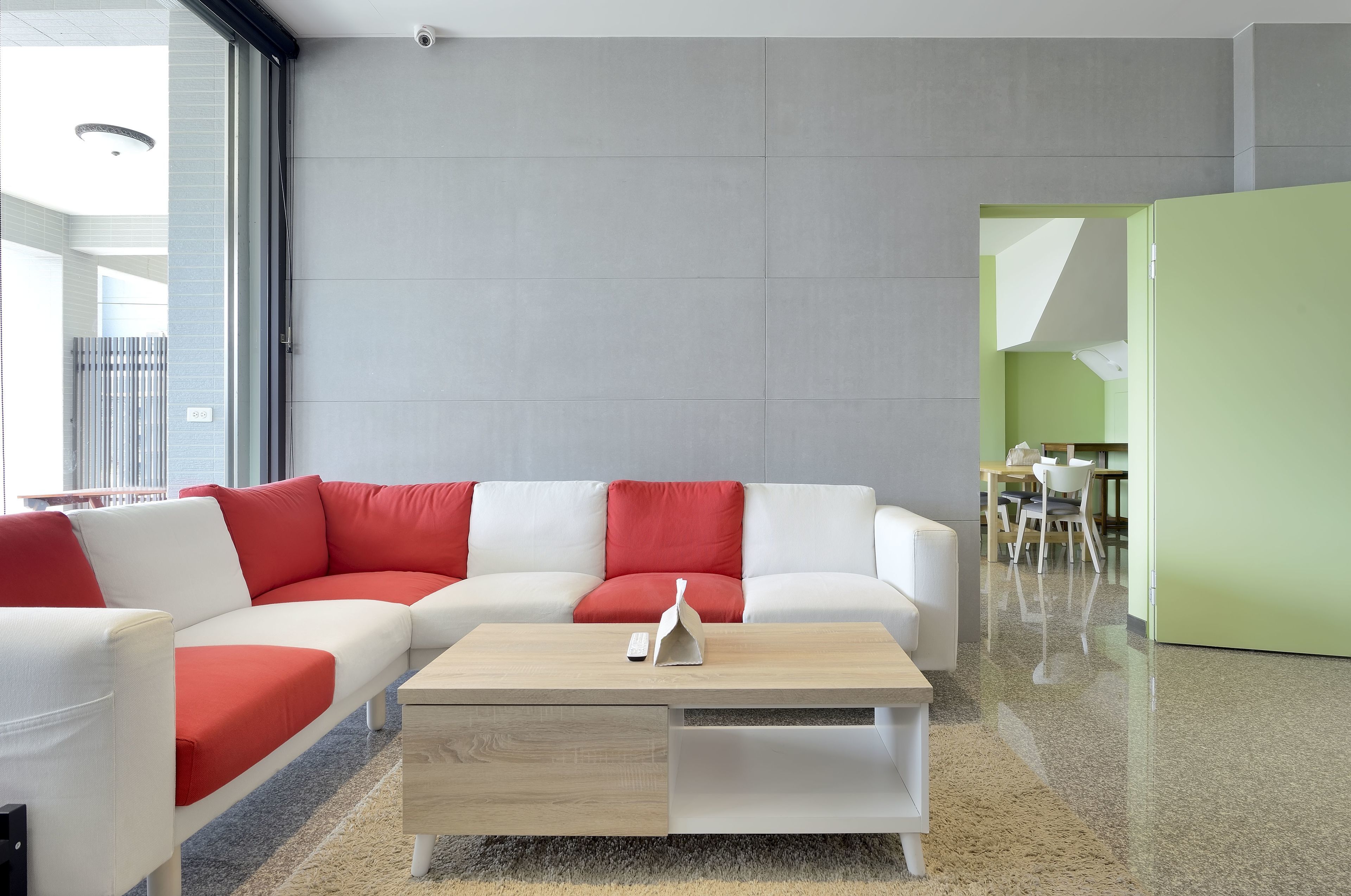 A modern living room with a white sectional sofa, red cushions, a wooden coffee table, and a green accent wall.