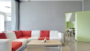 A modern living room with a white sectional sofa, red cushions, a wooden coffee table, and a green accent wall. - GOODHOUSE (Hengchun)
