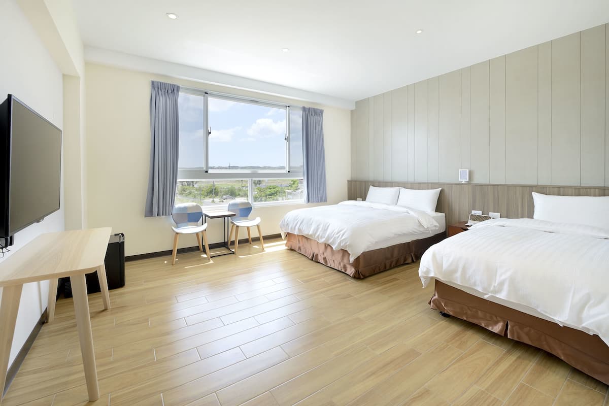 A hotel room with two beds, a desk with a chair, a TV, and a window with curtains.