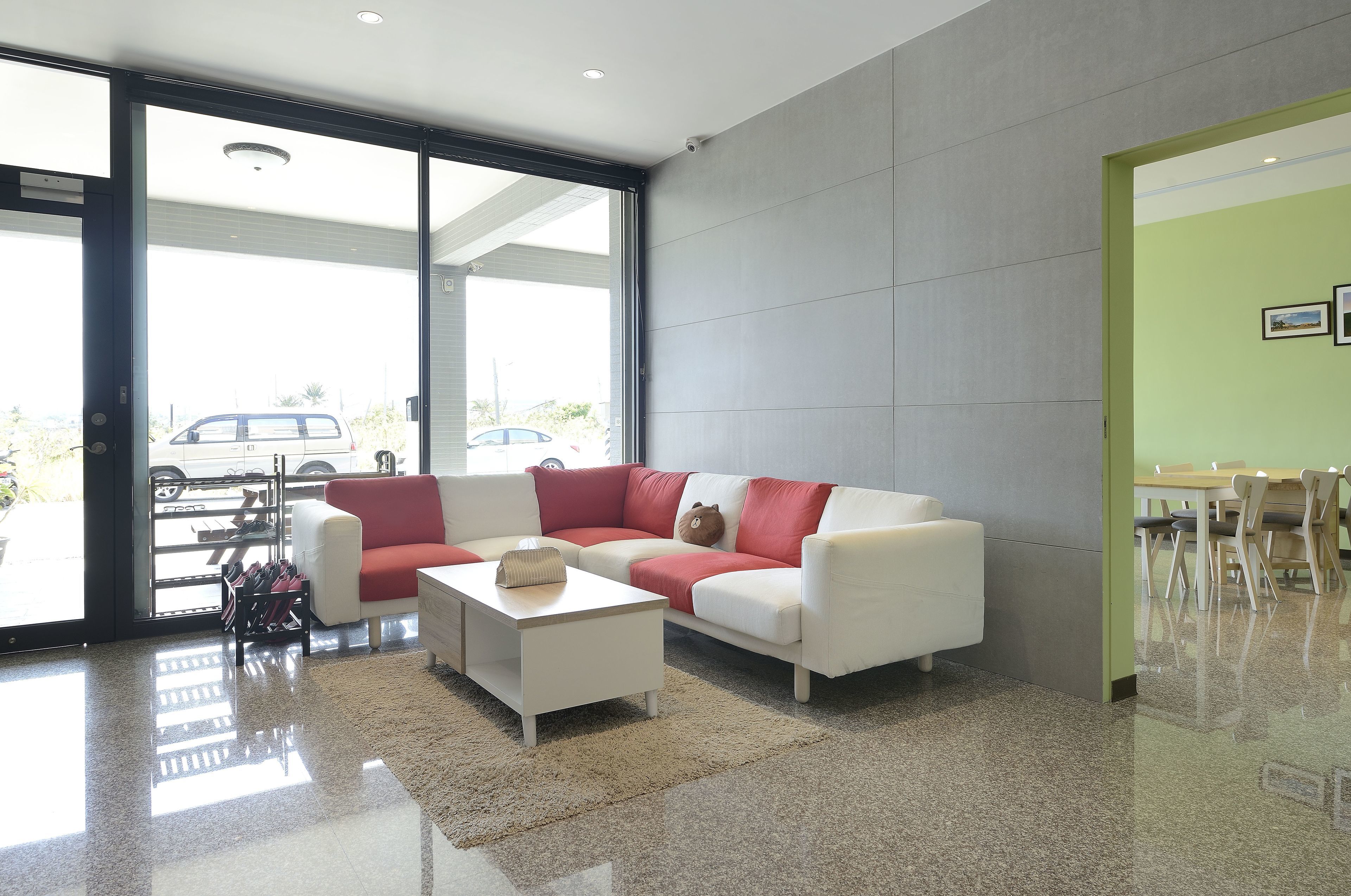 A modern living room with a white sofa, red cushions, a white coffee table, and a glass door leading to a parking area.