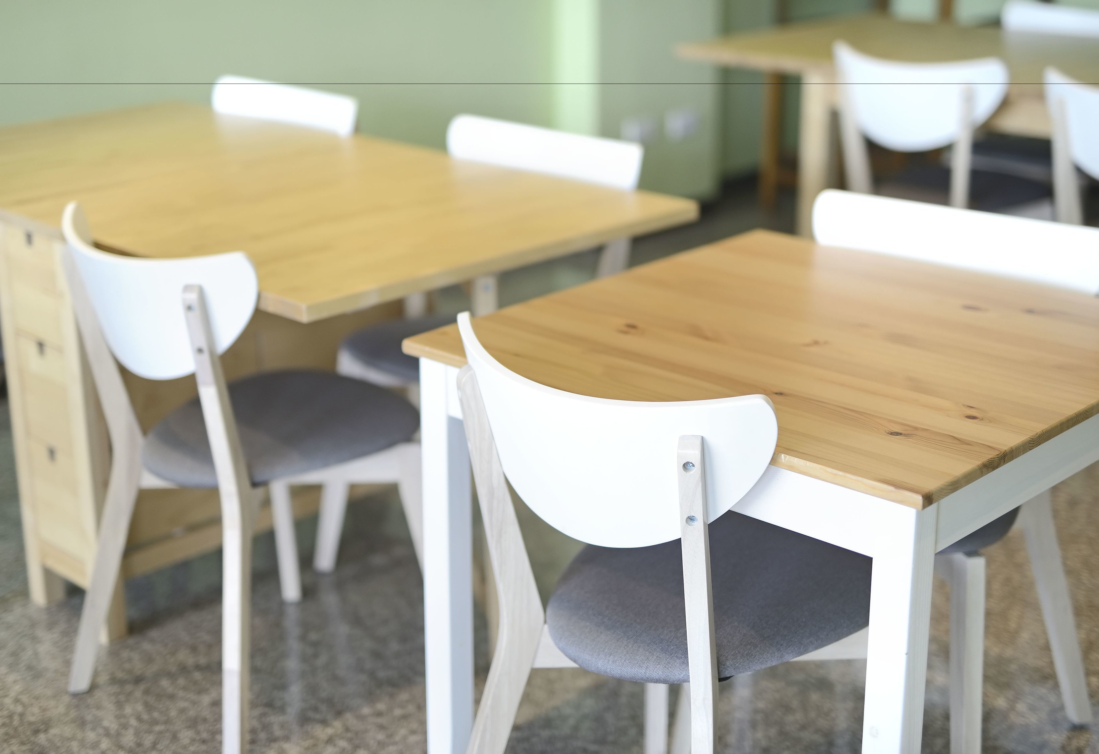 A classroom with wooden tables and white chairs.
