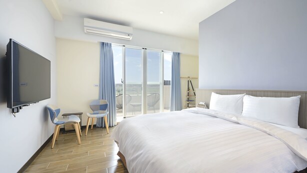 A hotel room with a large bed, a flat-screen TV, a small table with chairs, and a balcony with a view. - GOODHOUSE (Hengchun)