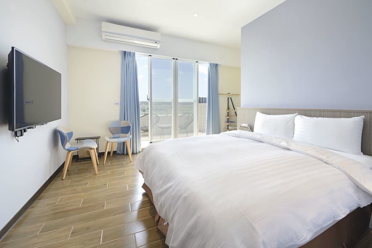 A hotel room with a large bed, a flat-screen TV, a small table with chairs, and a balcony with a view.