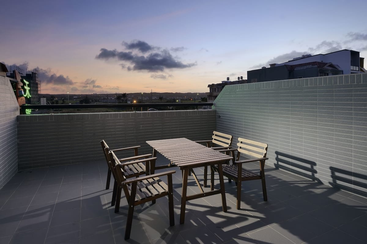 A rooftop terrace with a table and chairs, a view of the cityscape, and a tiled wall.
