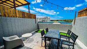 A patio with a table and chairs, a small round table, a cushioned bench, and a pool in the background. - GOODHOUSE (Hengchun)