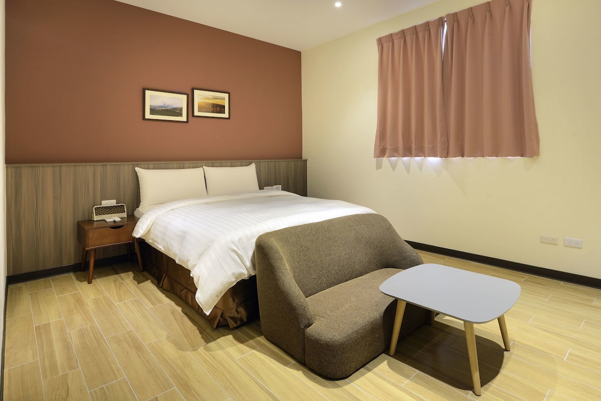 A bedroom with a bed, bedside table, and a small armchair with a table.