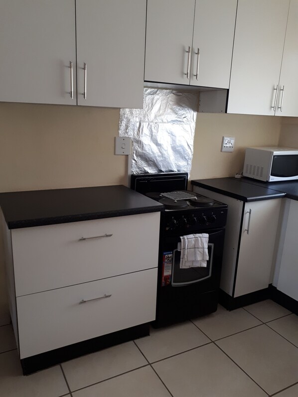 A kitchen with white cabinets, a stove, an oven, a microwave, and a tiled floor. - Esilulwini Ld Country Lodge (Manzini)