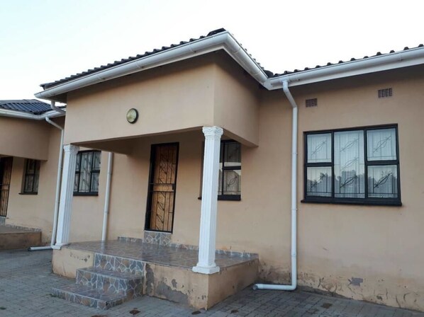 A beige building with a tiled roof, a front porch with steps, and a large window with multiple panes. - Esilulwini Ld Country Lodge (Manzini)
