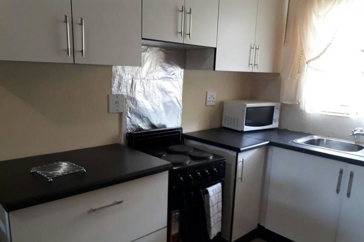 Una cocina con armarios blancos, una encimera negra, un microondas, una estufa y un lavabo.