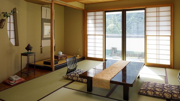 A tatami mat room with a low table, cushions, a traditional Japanese screen, and a sliding door. - Kinugawa Kokusai Hotel (Nikko)