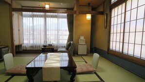 A traditional Japanese room with tatami flooring, a low table with a table runner, a sofa, and a view through shoji screens. - Kinugawa Kokusai Hotel (Nikko)