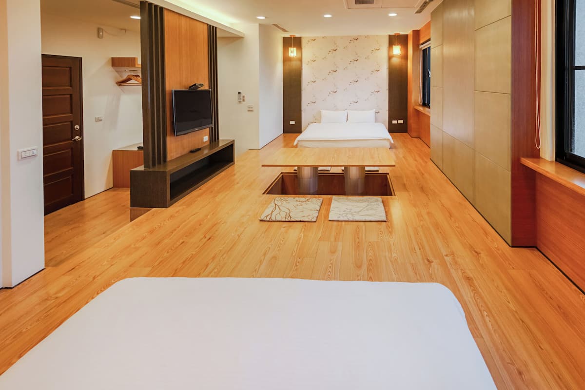 A hotel room with a wooden floor, a bed, a TV, and a window.