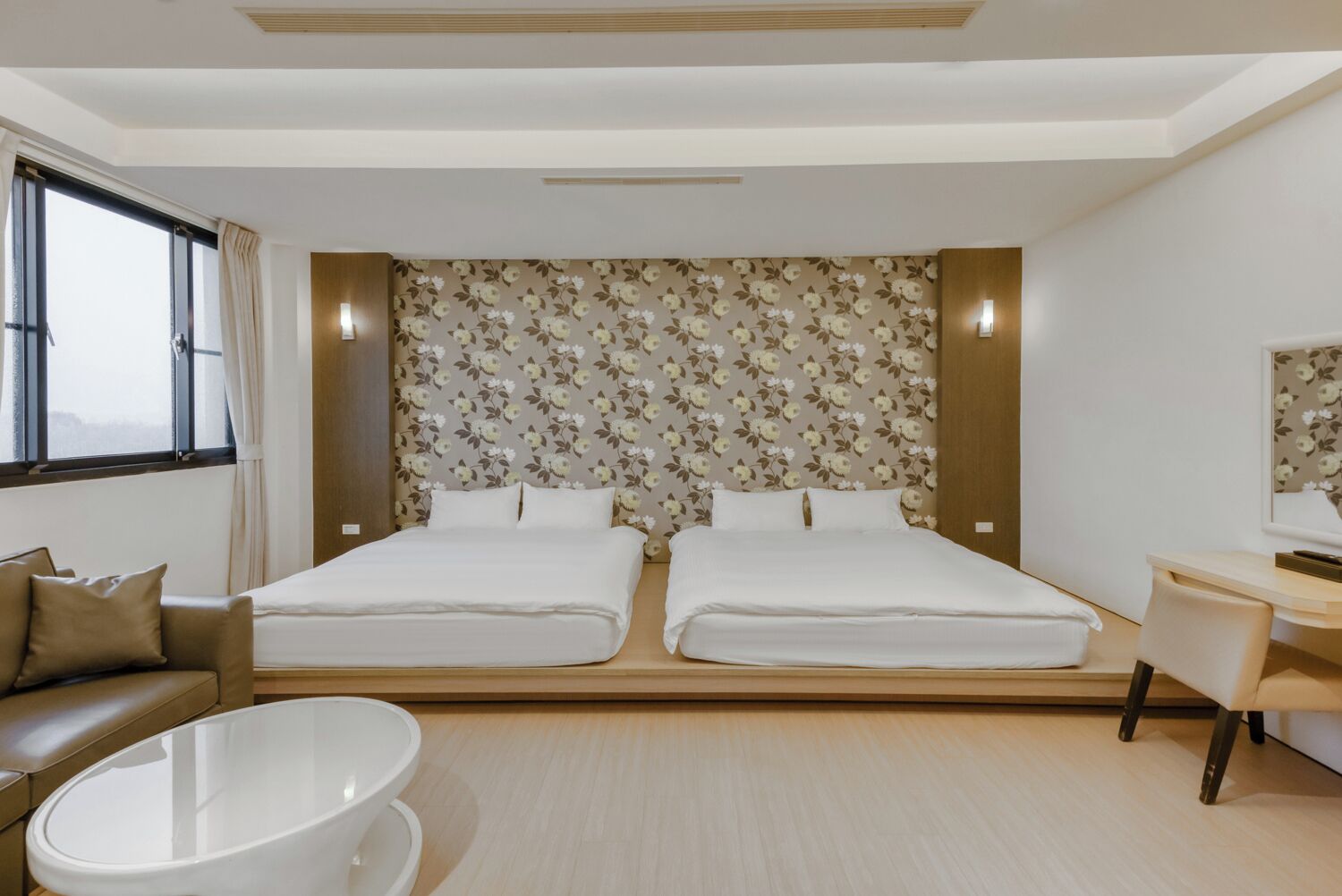 Ein modernes Hotelzimmer mit zwei Betten, einer Couch, einem Schreibtisch und einem großen Fenster.