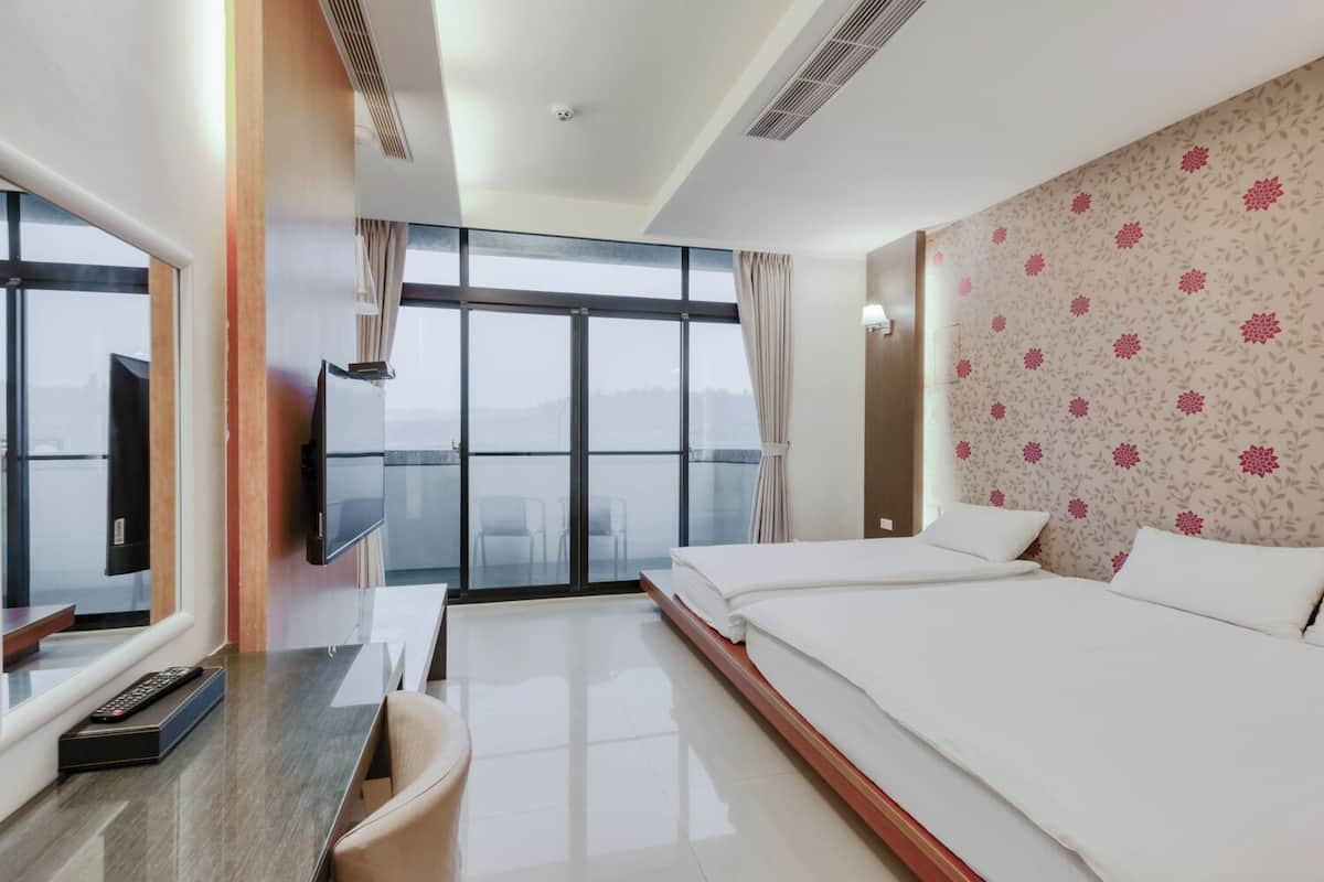 A hotel room with a large bed, a TV, a desk, and a view of the city.