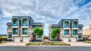 Un immeuble résidentiel moderne à l’architecture symétrique, doté de nombreux balcons, d’un garage et d’une pelouse bien entretenue.