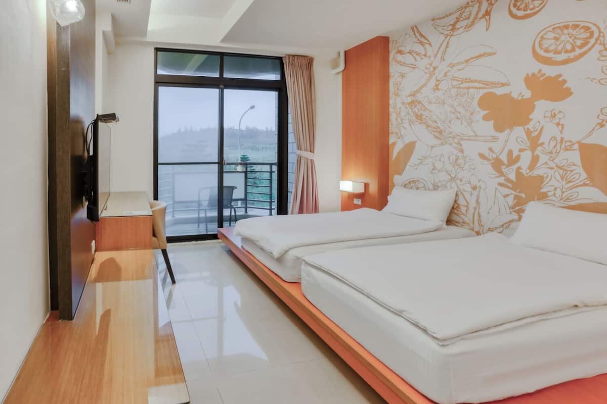 A hotel room with two beds, a desk, a chair, a window with a view, and a wall with a floral pattern.