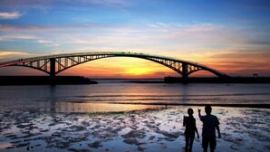 Un coucher de soleil sur une rivière, avec un pont.