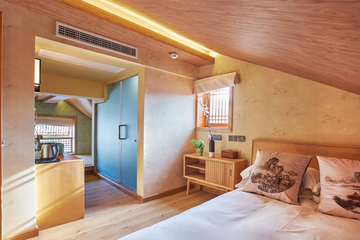 Een slaapkamer met een houten plafond, een bed met decoratieve kussens, een nachtkastje en een klein kastje.