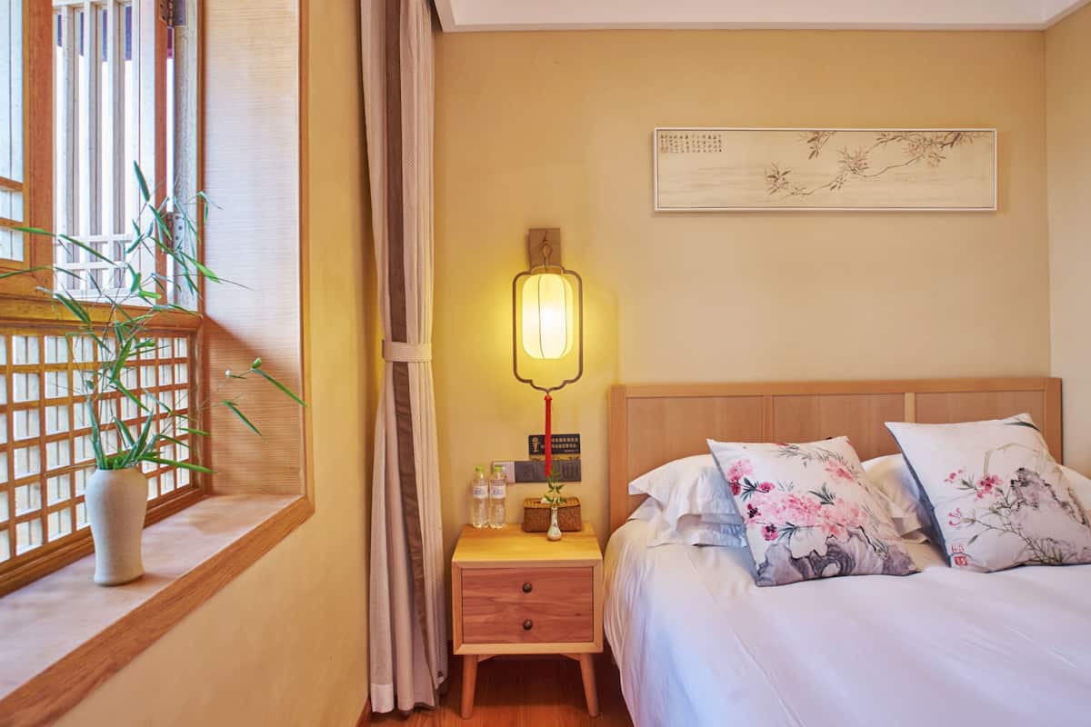 Een keurig opgemaakt hotelkamer met een bed, nachtkastje, lamp en een raam met een plant.